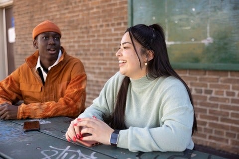A Black young man and a white young woman talking at a table