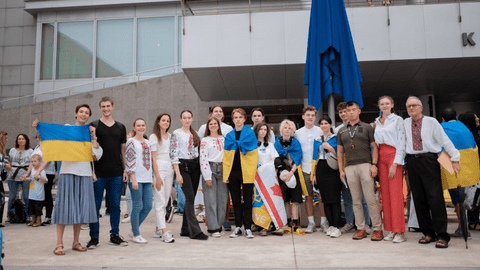 A group of students and adults pose in front of City Hall with Ukrainian flags