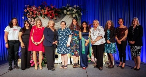 11 winners pose together on stage with flowers behind them. Credit Kinsella Marketing