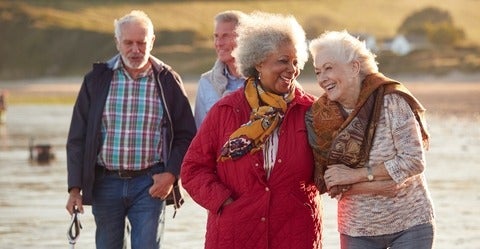 Four older adults walking on a beach