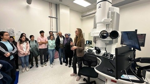 group of students and scientists look at an advanced microscope