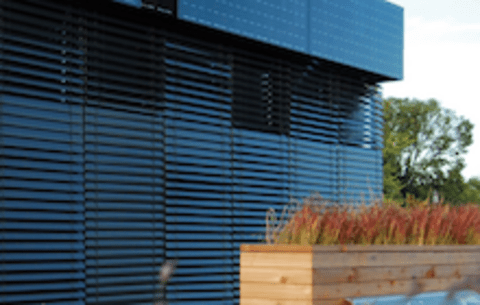 A view of black siding and solar panels with a natural grass garden in front