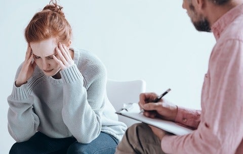 Woman with head in hands as therapist writes notes