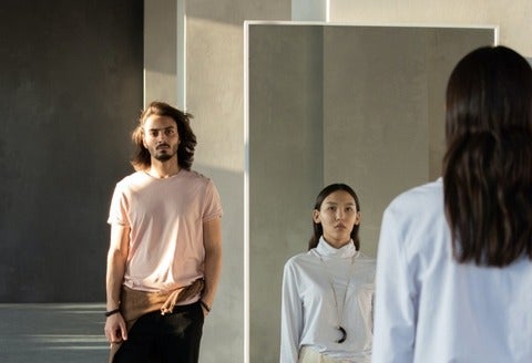 woman looks at herself in the mirror and man stands beside the mirror