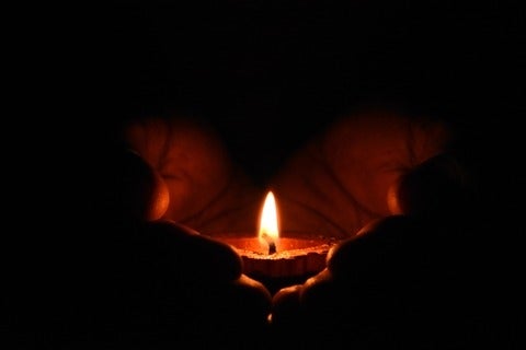 two hands cradle a lit candle