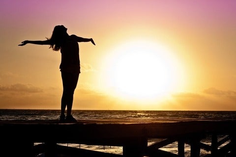 Woman in silhouette standing with her arms outstretched towards the sky.