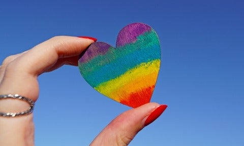 hand holding heart shaped wood peice with rainbow colours