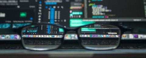 Black glasses on laptop with code in the back