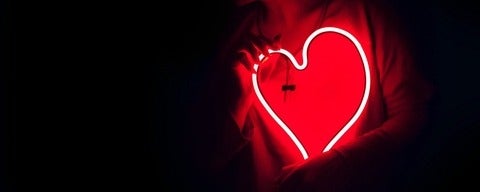 Glowing outline red outline of heart in the dark being held up by two hands