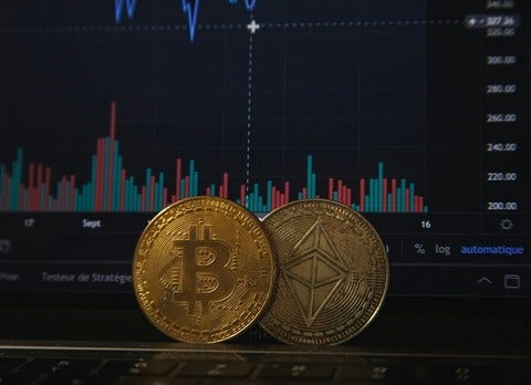 Bitcoin and Ethereum tokens in front of a computer screen with financial data