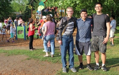 Waterloo Engineering students (left to right) Adam Rywak, Rodrigo Santalla and Daniel Qi pose while kids swarm a new playground structure at Keatsway Public School.