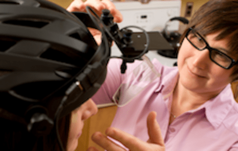 Christine Purdon adjusting a camera mounted on a helmet being worn by a young woman.