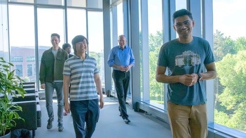 Dr. Norbert Lütkenhaus and group of PhD students and researchers walking through a building