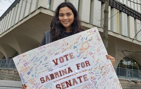 Sabrina holds up a sign covered in signatures that says "Vote Sabrina for Senate"