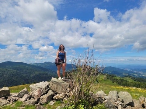 Samantha Kremer is standing on a rock with surrounding mountains in the background.  