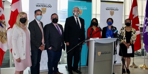 Ministers and researchers stand in front of podium and flags