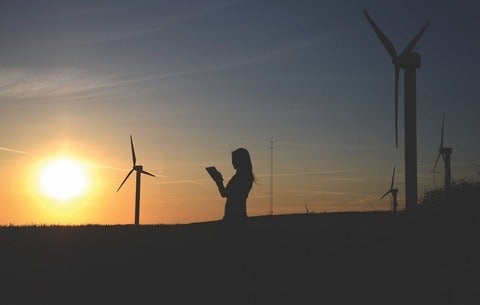 Someone reading with windmills and the sun in the background 