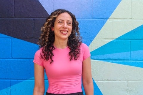 Artist Stephanie Boutari stands in front of a colourful mural and smiles