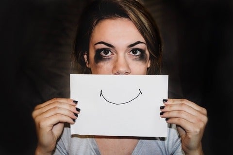 Woman with smudged mascara on her eyes holding a piece of paper with a smile that covers her mouth