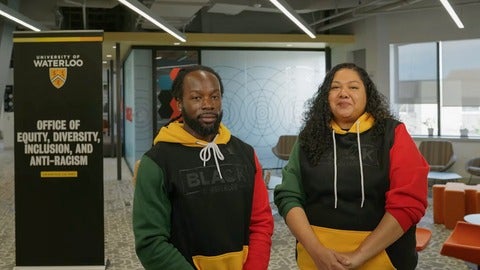 Dr. Christopher Taylor and Jennisha Wilson standing inside the EDI-R office wearing their Black at Waterloo hoodies
