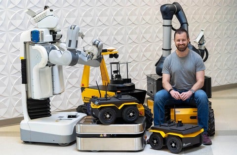 Ryan Gariepy sits among a bunch of Clearpath robots in front of a textured wall
