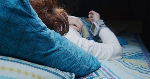 A person in bed checking their blood pressure with a wrist monitor.