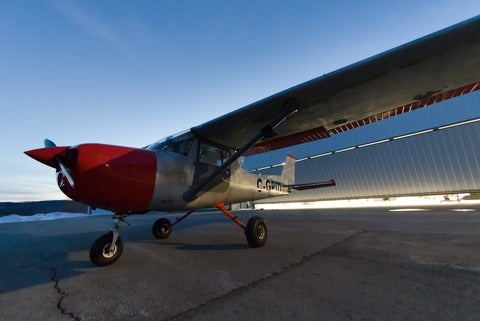 Small red and white plane parked at hanger