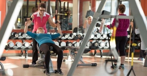 Gym setting with woman on bench press, one assisting, and one to the side
