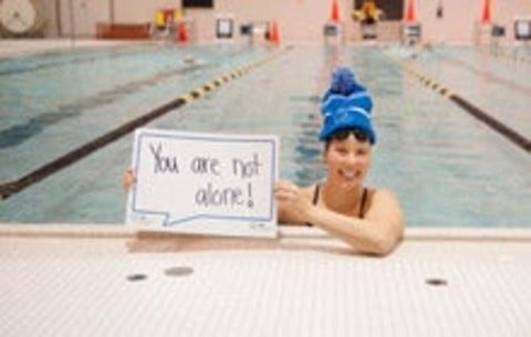 Waterloo varsity swimmer holding sign that reads "You are not alone"