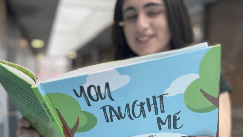 Talina holding the English cover of the childrens book, You Taught Me,  featuring a blue sky background with soft clouds.