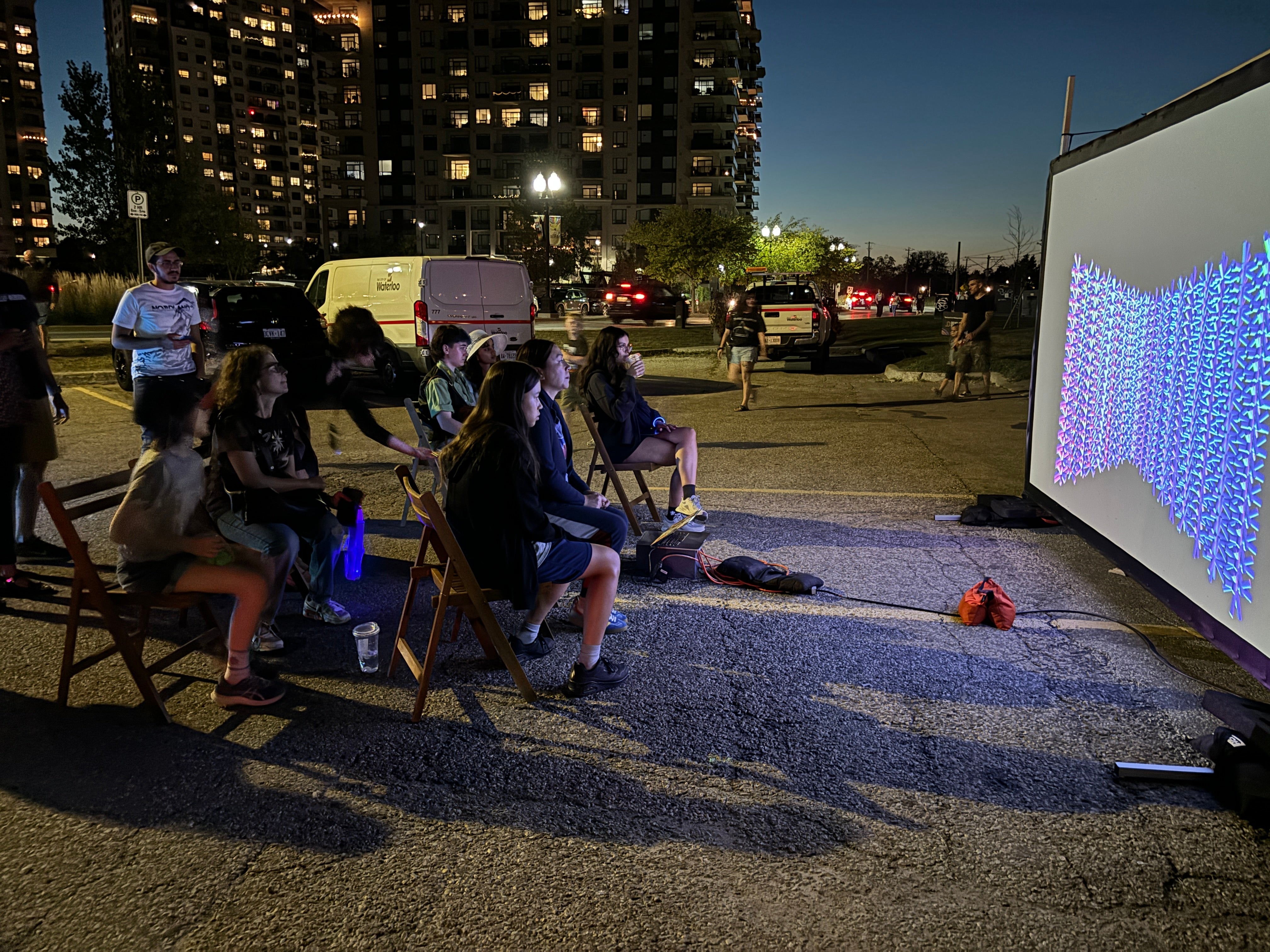 People standing outside a bus watching a piece of art on a projected screen