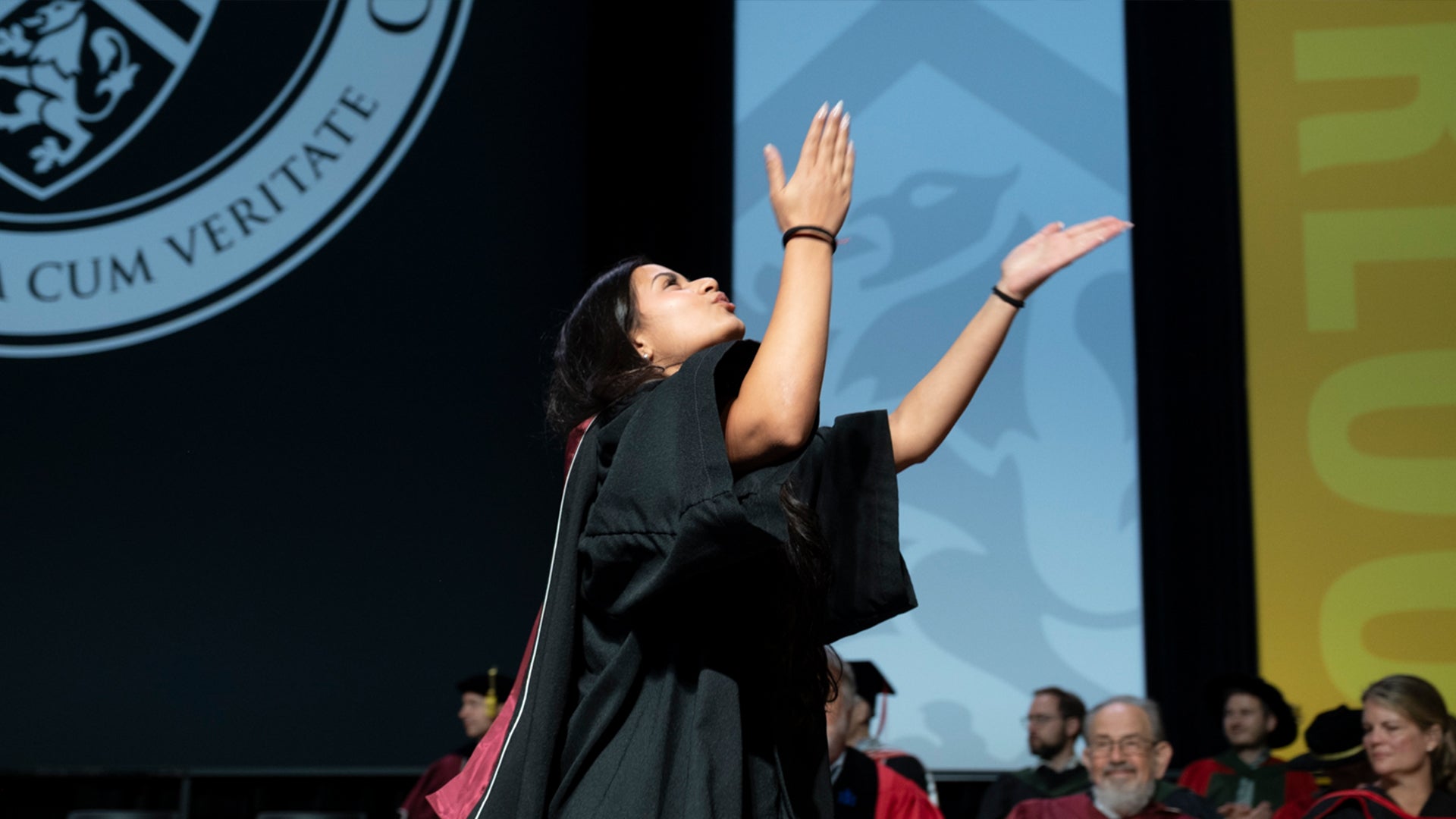 Graduate crosses stage and extends hands to the sky