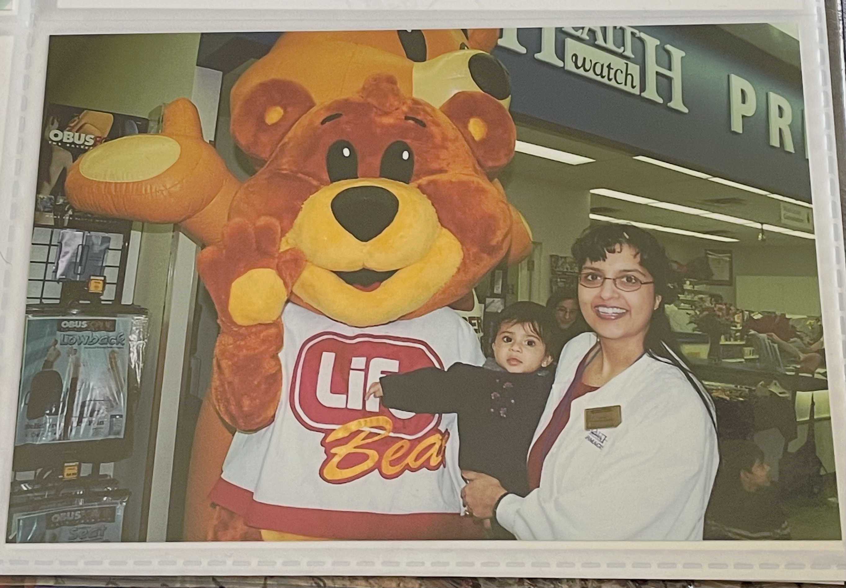 Baby Sapna Tripathi being held by her mom wearing pharmacist's lab coat with mascots