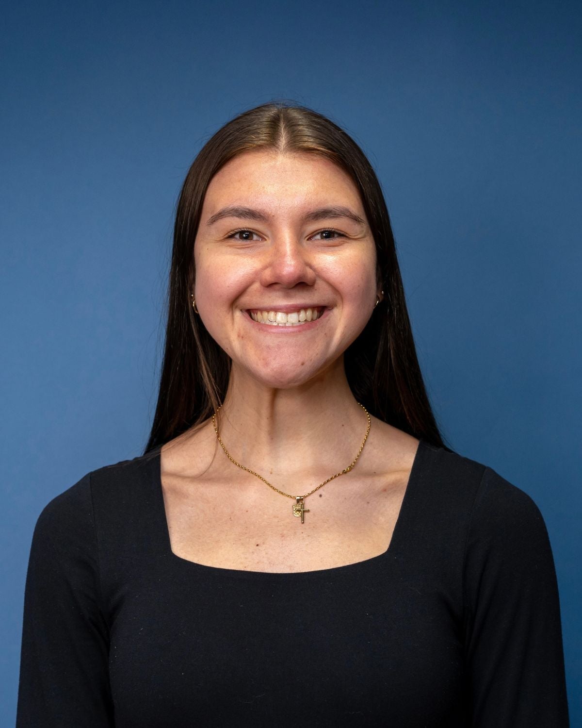 Viktoria is wearing a black long sleeve shirt and a gold necklace. She is against a blue backdrop.