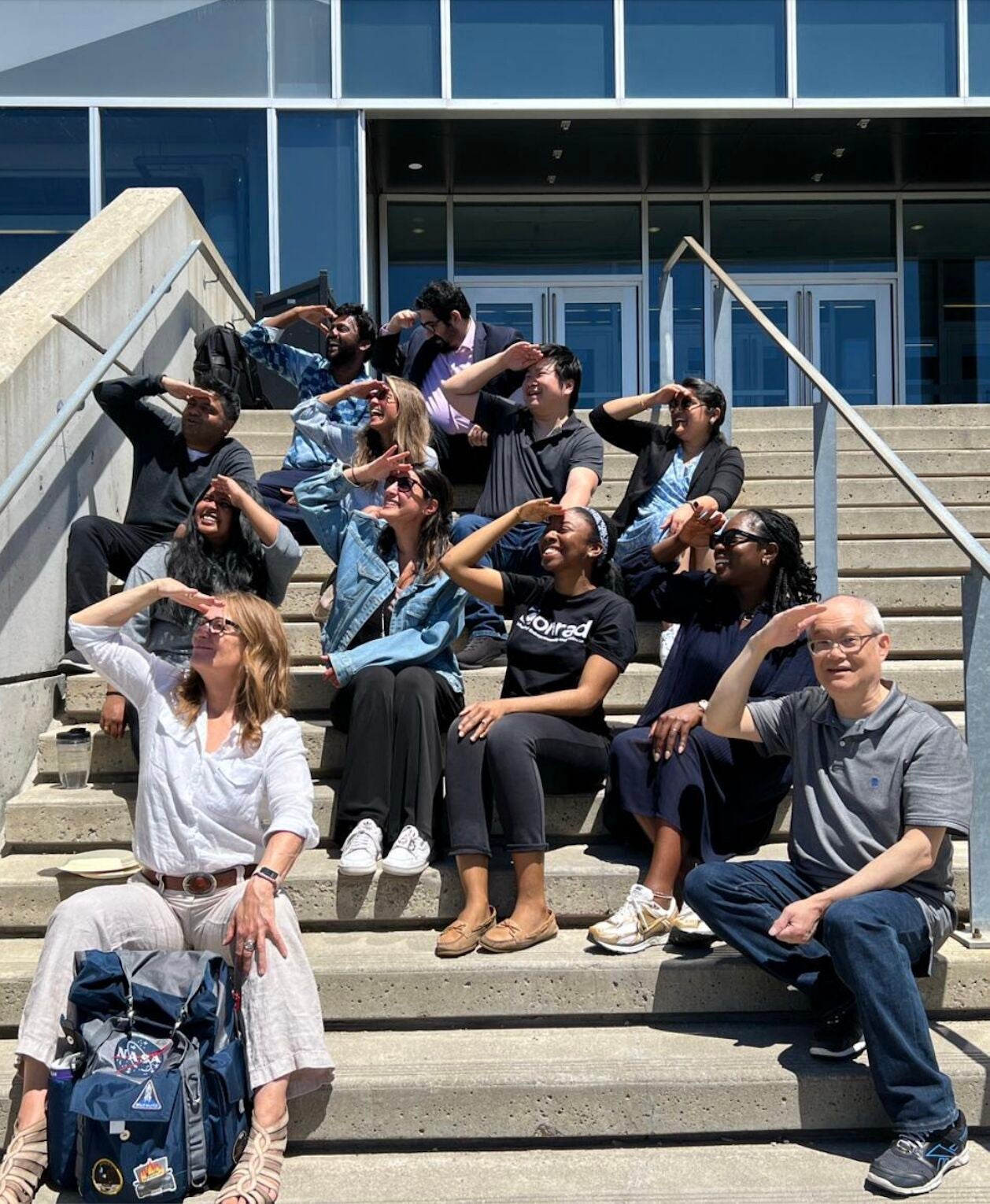 Wayne Chang sits on the steps of E5 with his students as they raise their hands to cover the sun from their eyes.