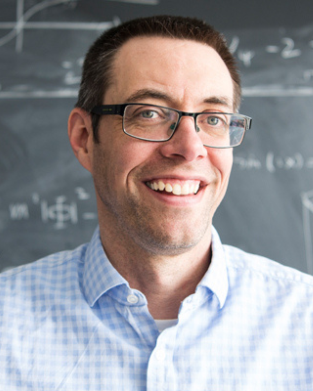 Headshot of Will Percival smiling. There is a blackboard with math equations behind him.