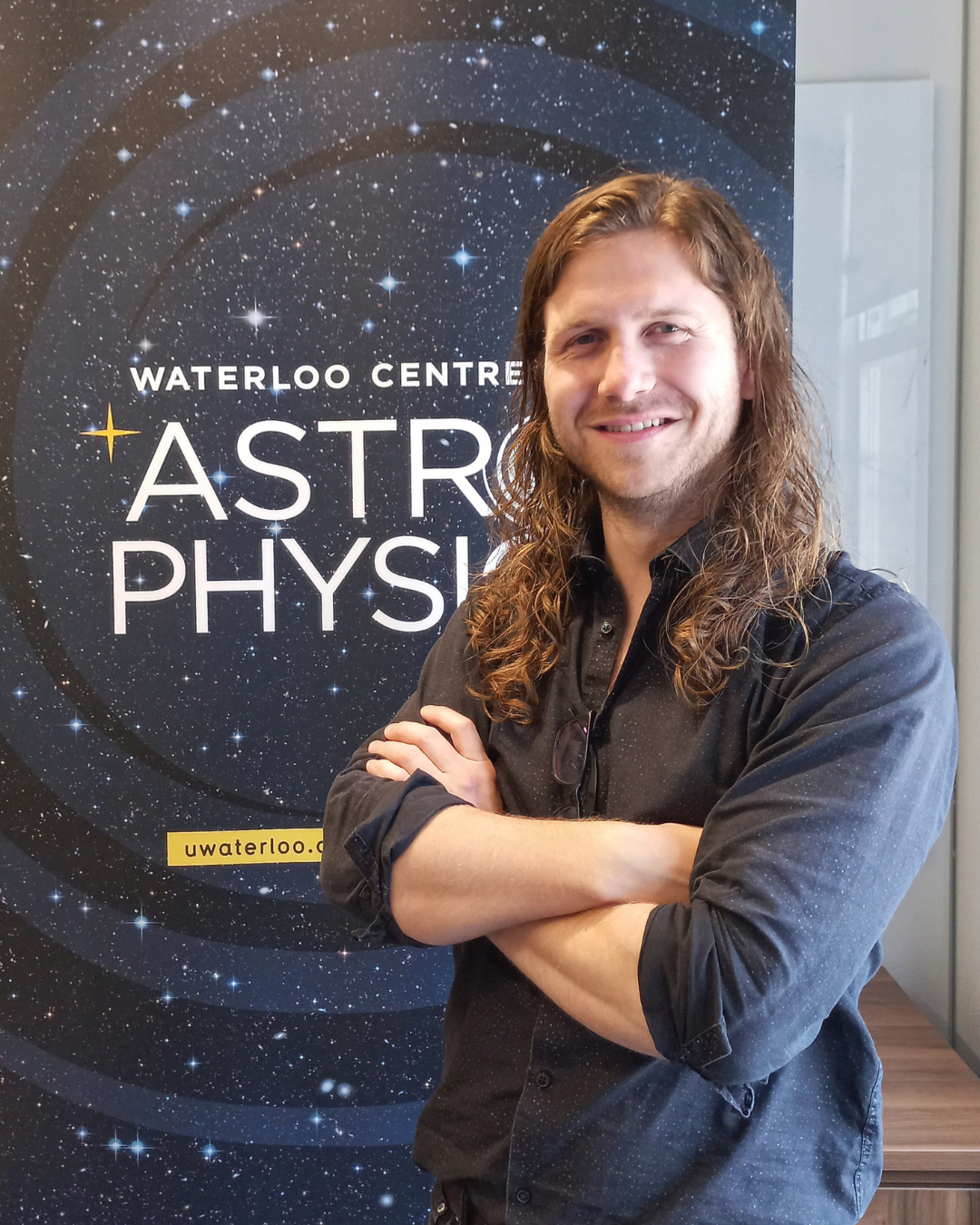 Roan Haggar standing with his arms crossed in front of a banner that says "Waterloo Centre for Astrophysics."