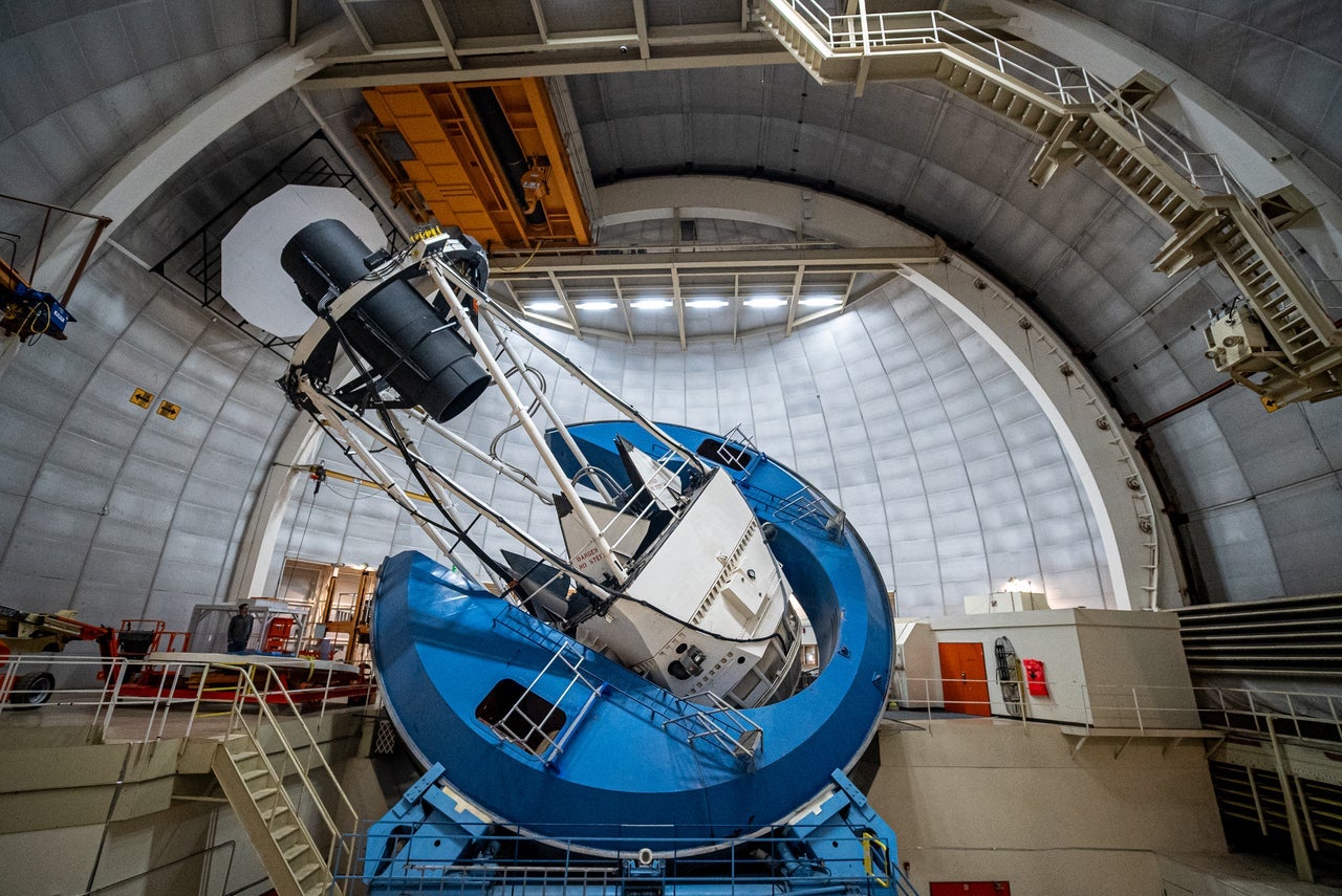 DESI’s instrument, a long black cylinder supported by the metal framework of the telescope, points at the domed ceiling