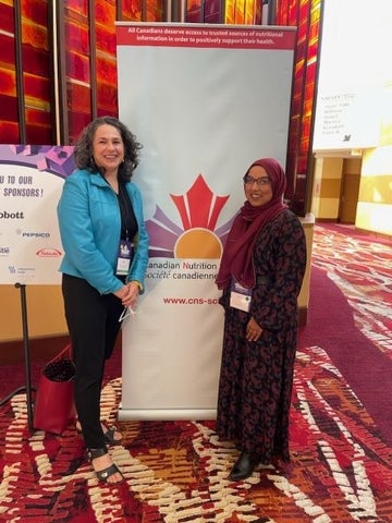 Heather Keller and Safura Syed standing in front of the CNS poster banner