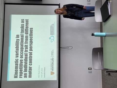 Nathalie Oomen standing in front of the slides for her dissertation presentation.