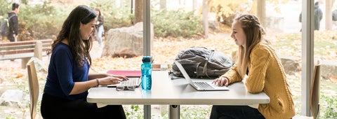 Two students sitting on each end of a table chatting