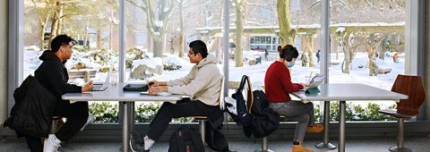 Two groups of students sitting at tables studying inside the QNC with a view of the winter scenery outside.