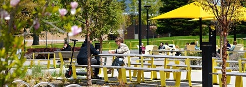 Students sitting outside in the arts quad at yellow picnic tables.