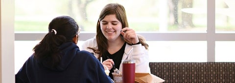 Two student talking, while sitting at a table.
