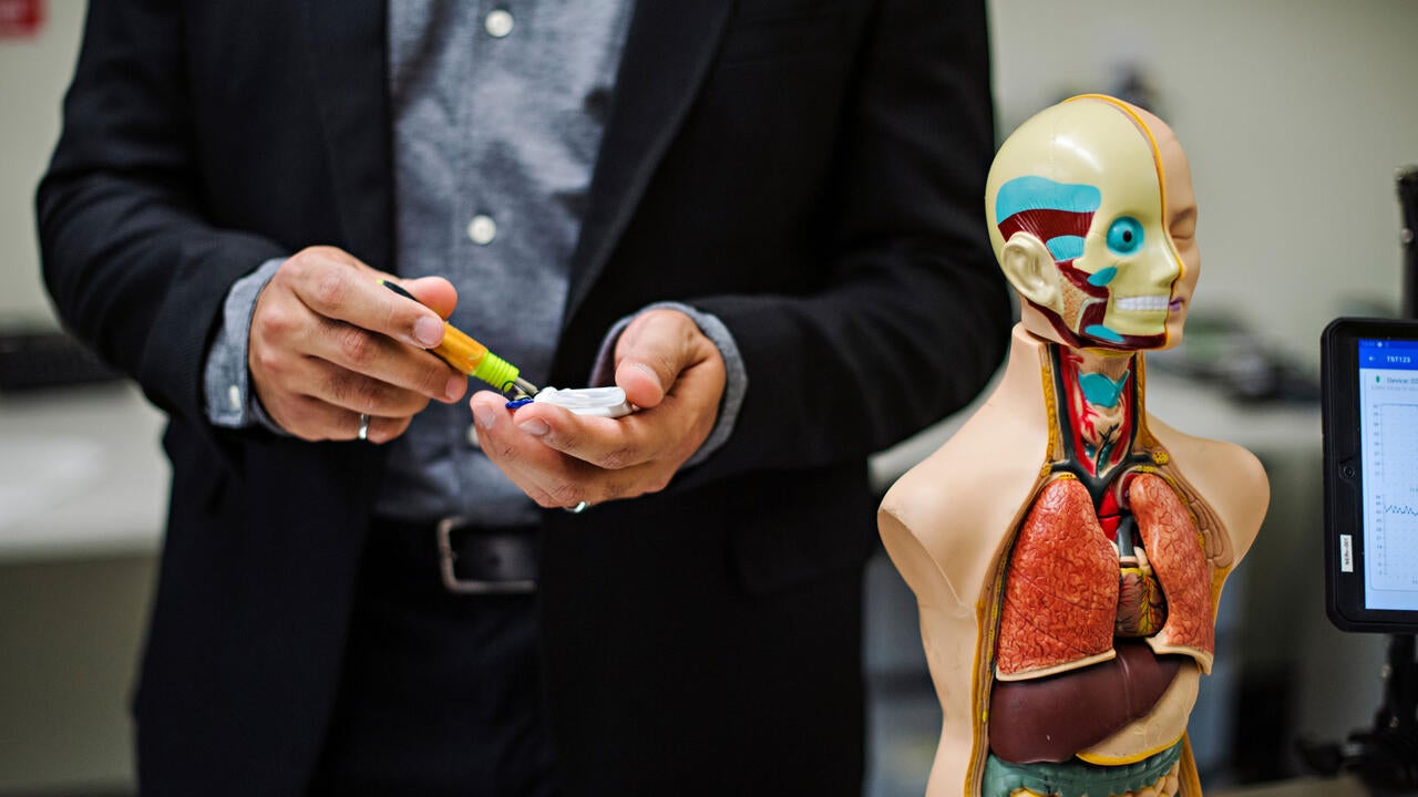 A person working on an electronic component while standing next to a human anatomy model