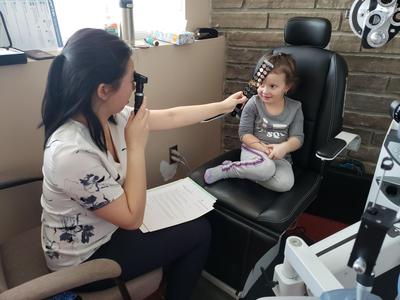 Rachel Ng looks through a retinoscope while holding a lens bar to the eye of a small girl.