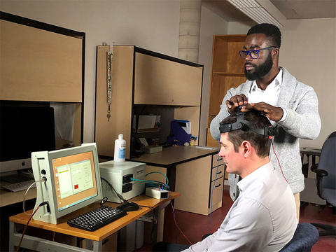 Richard Donkor looks at a computer monitor while adjusting Dr. Ben Thompson’s headset