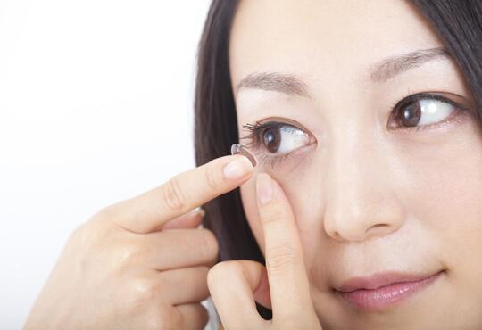 A woman inserts a contact lens into her eye