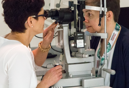 Optometry alumna examining another woman using a slit lamp