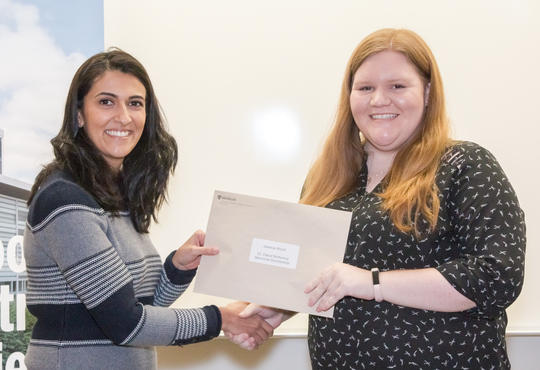 Dr. Shamrozé Khan smiles and shakes Jessica Wood’s hand as she passes Jessica an envelope.